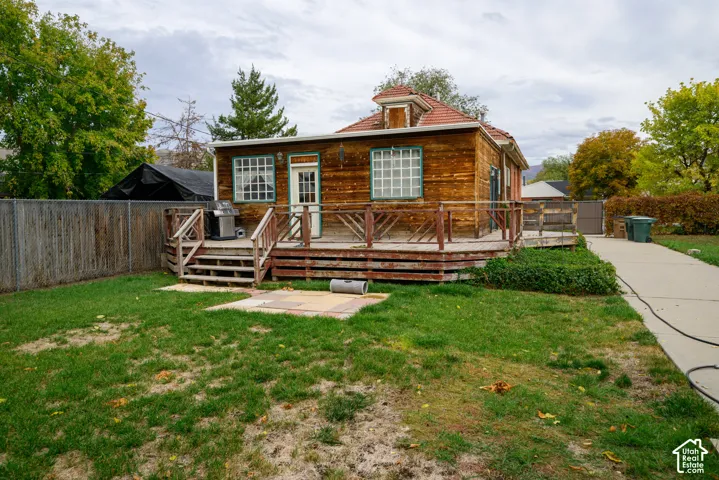 Exterior wood siding, elevated wraparound deck with wooden railings, and concrete driveway leading to the rear of the property