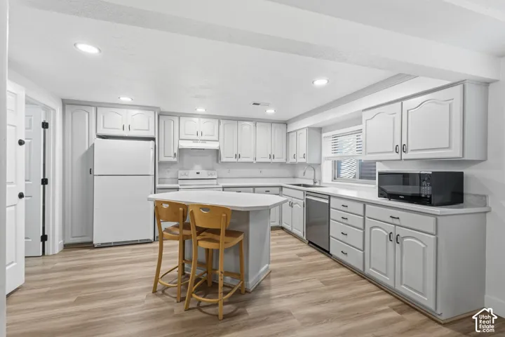 Kitchen featuring white cabinetry, wood-finish flooring, a central island with a stone-surface countertop, recessed lighting, and stainless steel dishwasher and large pantry.