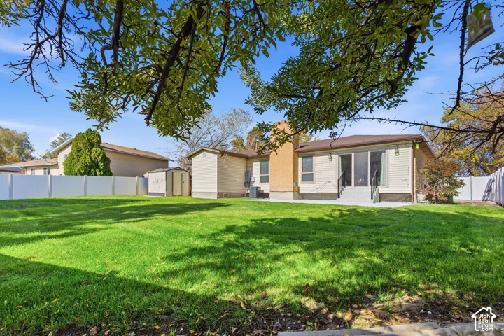 Expansive backyard featuring a level lawn with white vinyl fencing, a brick chimney, sliding glass patio doors and a storage shed