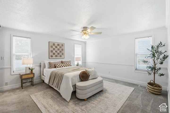 Neutral-toned room featuring wall-to-wall carpeting, wainscoting, a multi-blade ceiling fan with integrated lighting, and multiple windows