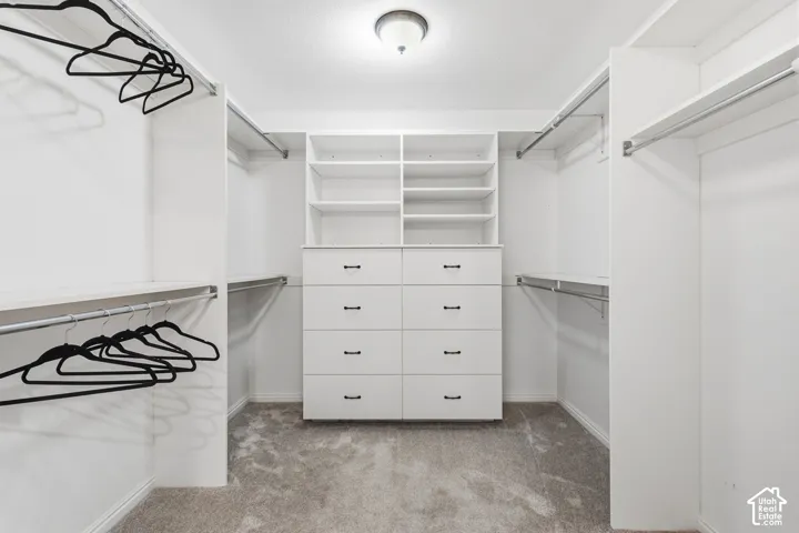 Walk-in closet featuring white built-in shelving, multi-drawer cabinetry with matte black hardware, dual-level hanging rods, and neutral carpeting