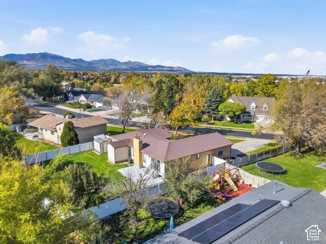 Aerial perspective featuring a residential property with a paved patio, perimeter fencing, and rooftop solar panels set against a mountain backdrop