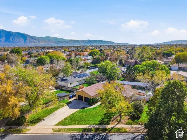 Aerial perspective of a single-story residence featuring a concrete driveway, two-car garage, roof-mounted solar panels, and mature landscaping