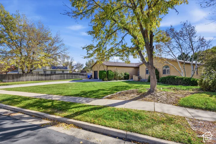 Single-story brick exterior featuring arched window detailing, an attached garage, and a mature tree-lined front lawn