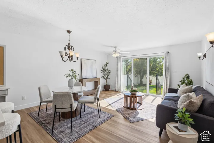 Open-concept living space featuring wood-finish flooring, a dining chandelier, a ceiling fan with integrated lighting, wall-mounted sconce lighting, and sliding glass doors
