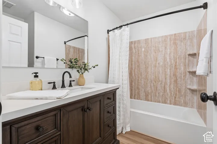 Bathroom featuring a dark wood-finish vanity with a light-toned countertop, oil-rubbed bronze plumbing fixtures, a full-width wall mirror, and a tub-shower combination with integrated shelving
