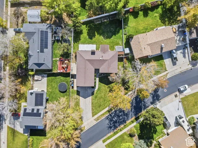 Aerial perspective of a property featuring an L-shaped structure, asphalt-shingled roof, concrete driveway, and a fenced rear yard