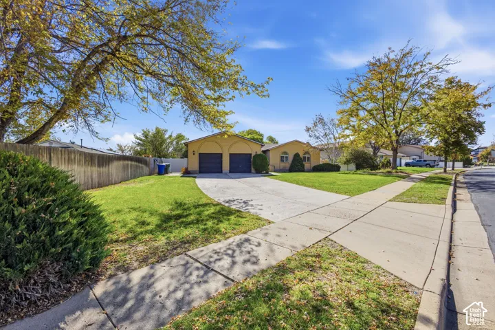 Single-story exterior featuring a stucco facade, arched entryway detailing, attached two-car garage, concrete driveway, and mature landscaping