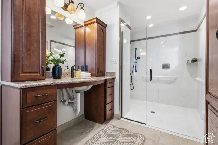 Bathroom featuring a vanity with wood-finish cabinetry, stone countertop, glass-enclosed shower with tiled surround that is wheelchair accessible, and integrated lighting fixtures
