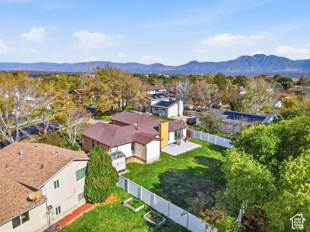 Aerial perspective featuring a multi-level residence with a composition shingle roof, a dedicated concrete patio, a fenced backyard, and mountain range scenery