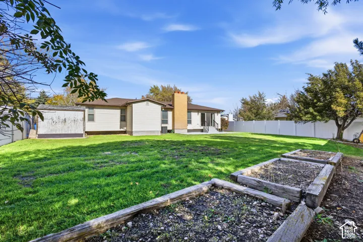 Expansive backyard featuring a lawn, timber-framed planting garden beds, and white vinyl fencing.