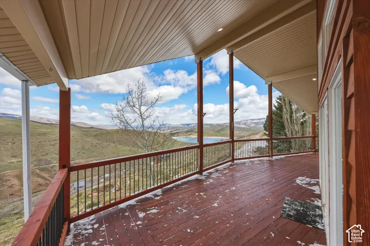 Covered wraparound wooden deck with metal railings, recessed ceiling lighting, and expansive mountain and water scenery