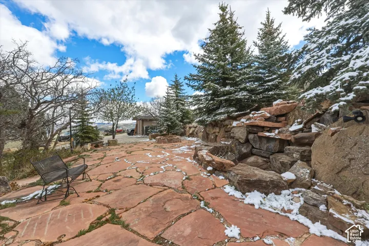Flagstone patio featuring a built-in stone fire pit, integrated rock retaining wall, and mature coniferous landscaping