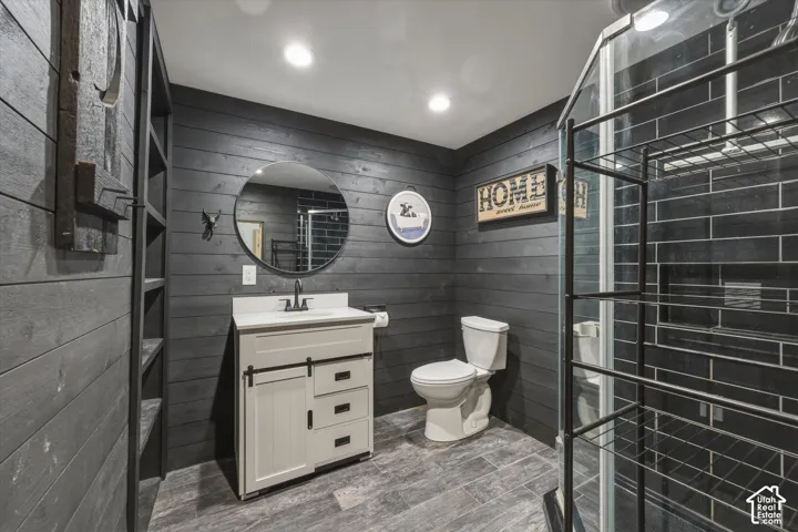 Bathroom featuring black wood-plank walls, a vanity with a sliding barn-door style cabinet, a circular wall-mounted mirror, and a walk-in shower with dark subway tile surround