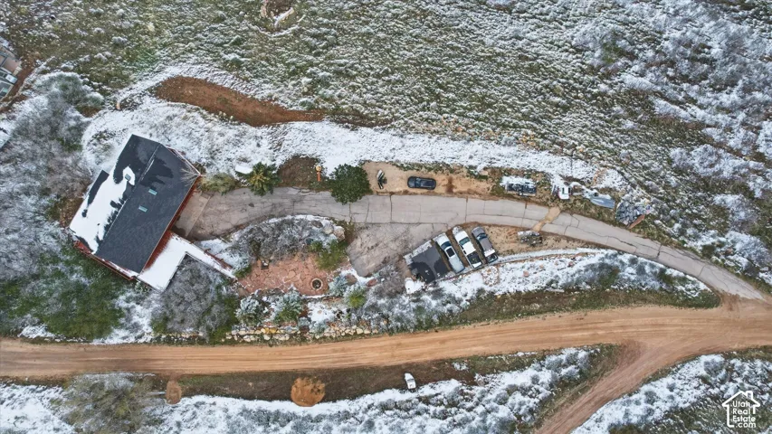 Aerial perspective featuring a multi-level structure with a dark shingle roof, a paved driveway, and a stone-paver patio area
