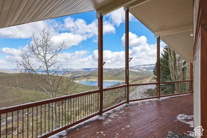 Covered wraparound wooden deck featuring vertical support beams, metal railing, and expansive mountain and water scenery