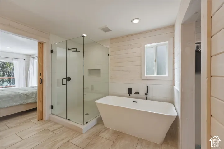 Bathroom featuring a freestanding soaking tub, walk-in glass-enclosed shower with matte black fixtures, recessed shower niche, light wood-finish horizontal plank wall paneling, and tile flooring