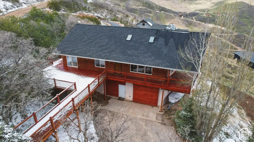 Multi-level structure featuring a wood-clad exterior, shingle roofing, dual skylights, an expansive elevated wooden deck with railing, and a ground-level concrete patio