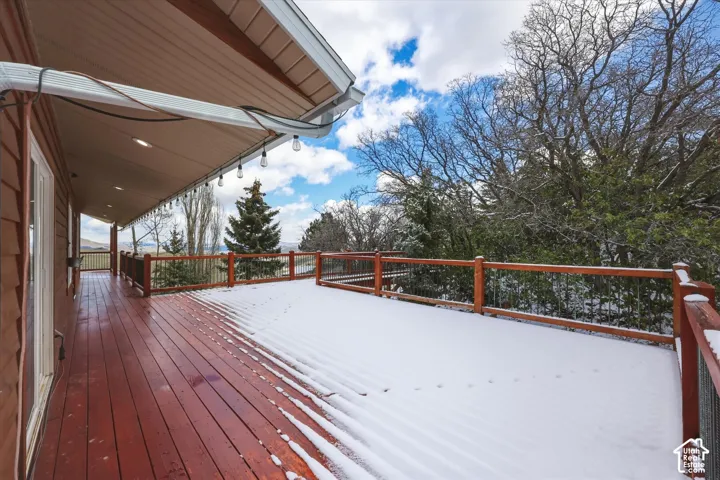 Expansive covered deck with wood-finish decking, wood railing, metal balusters, and recessed ceiling lighting