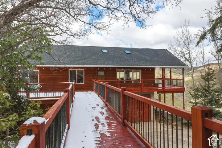 Multi-level home exterior featuring a wooden-railed elevated walkway, expansive wraparound deck with metal balusters, cedar siding, and two roof-mounted skylights