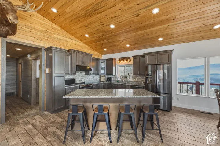 Kitchen featuring vaulted wood-plank ceiling, recessed lighting, stone-finish countertops, central island, and wood-finish tile flooring