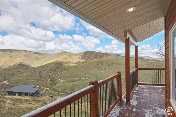 Covered deck featuring wood-finish decking, dark metal railings, recessed lighting, and a landscape backdrop