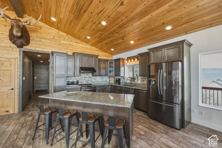 Kitchen featuring vaulted wood-plank ceilings, dark wood cabinetry, stone-surface countertops, stone tile backsplash, and recessed lighting