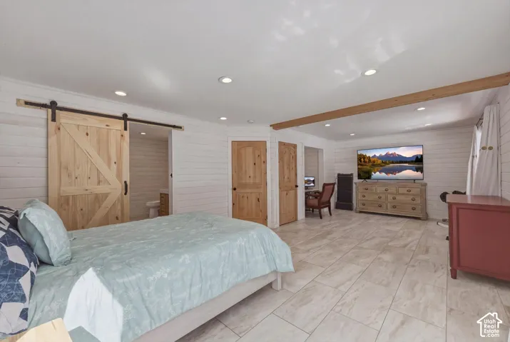 White horizontal shiplap walls, light-toned stone-finish tile flooring, recessed ceiling lighting, rustic wood-finish barn door on a black iron track, and exposed wooden ceiling beam