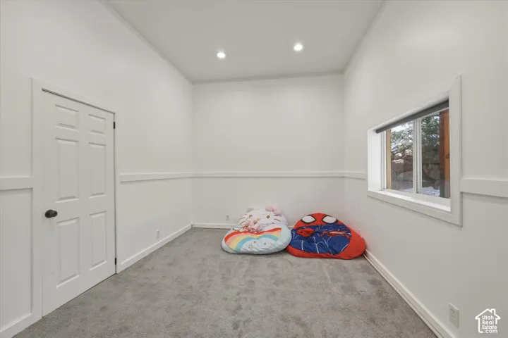Interior room featuring high ceilings, neutral carpet flooring, wainscoting, recessed lighting, and a window with a white frame