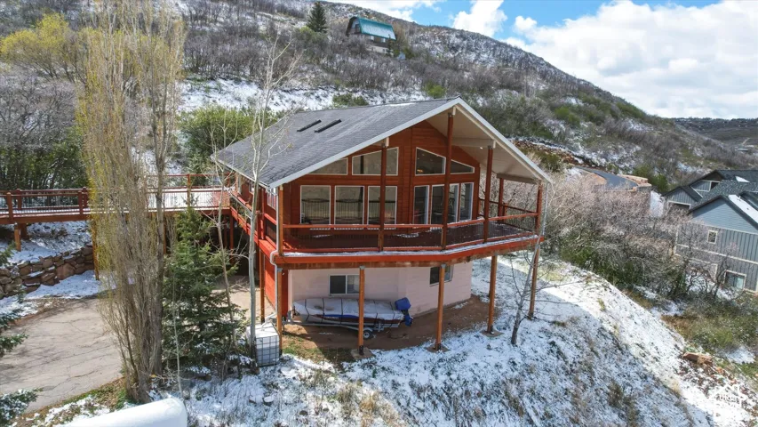 Multi-level wood-exterior structure featuring a wrap-around elevated deck, expansive multi-pane windows, dual roof skylights, and a natural hillside setting