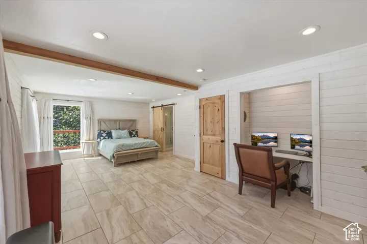 Interior space featuring shiplap wall paneling, large-format tile flooring, a recessed built-in workstation, a wood-finish sliding barn door, and a decorative exposed timber ceiling beam