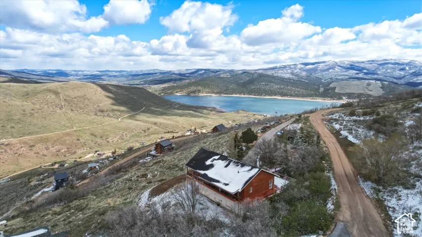 Aerial perspective featuring a wood-sided structure with an elevated deck, mountain backdrop, and lake scenery