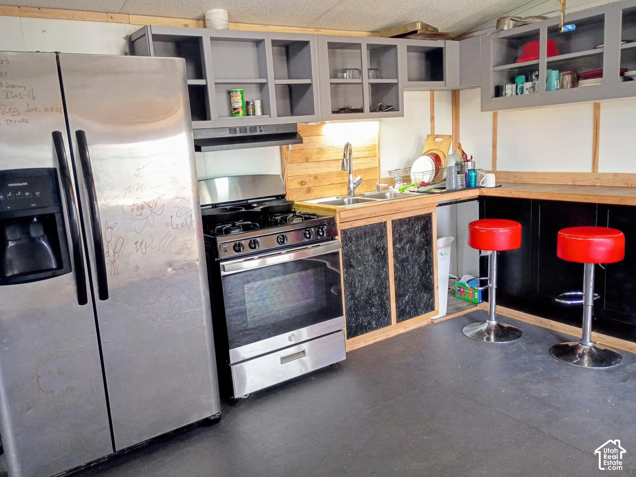 Stainless steel refrigerator, gas range, wood-finish wall paneling, dual-basin sink with pull-down faucet, and built-in cabinetry with glass-panel doors