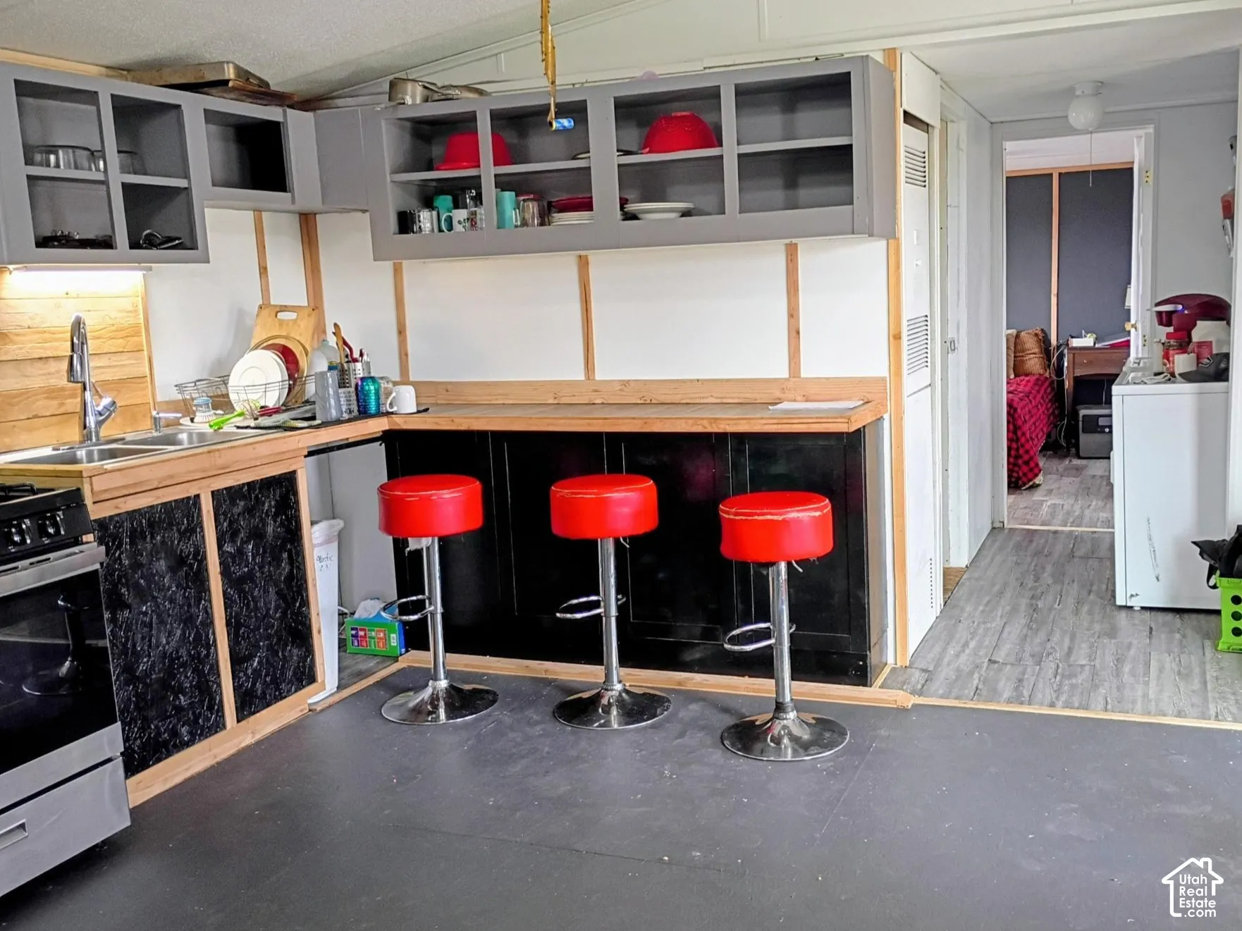 Kitchen featuring grey upper cabinetry, black lower cabinetry, stainless steel sink with metal faucet, and wood-finish countertop with integrated breakfast bar
