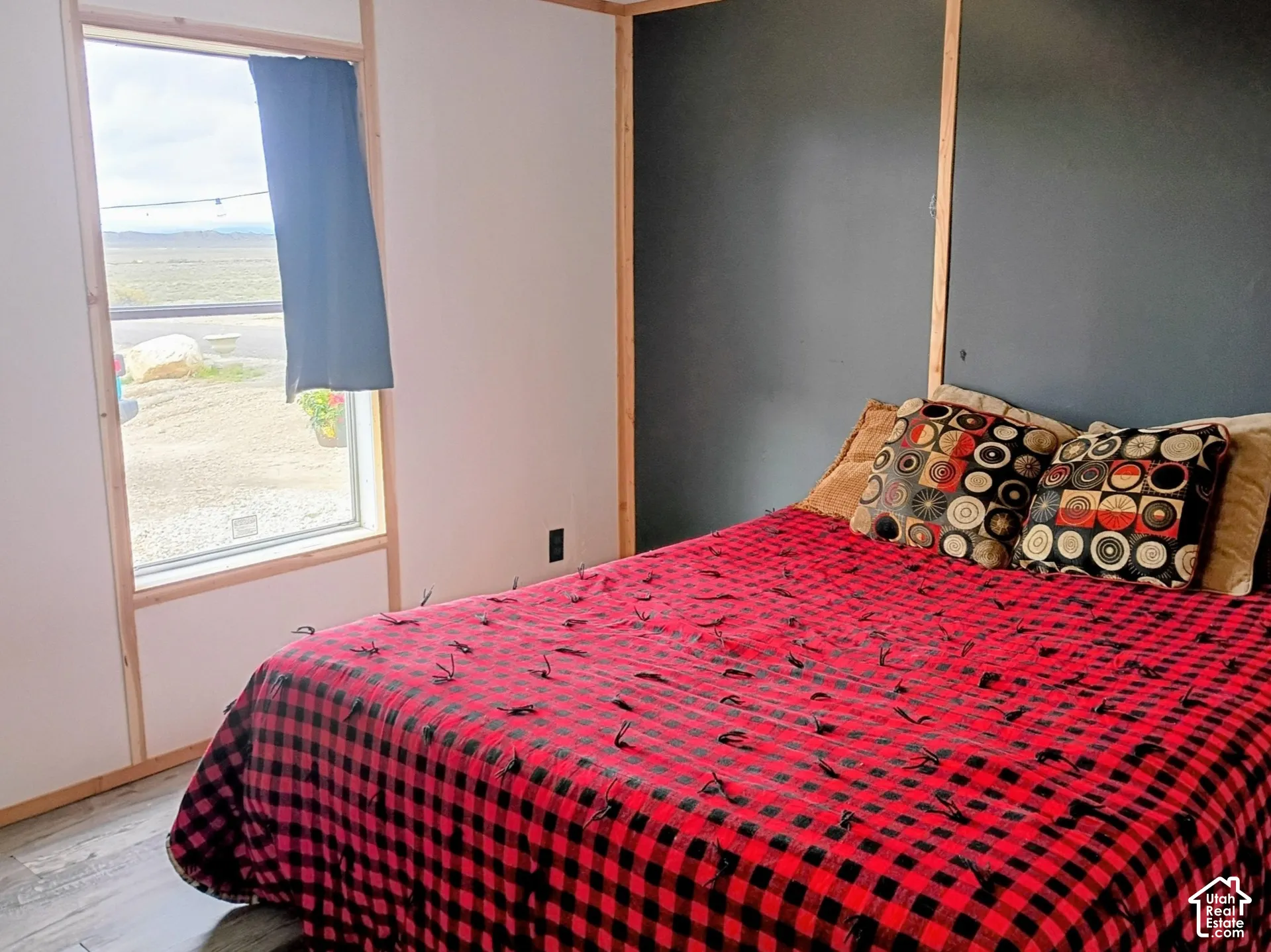 Master bedroom featuring wood-finish flooring, charcoal-toned accent wall, light-toned wood trim, and a window with exterior landscape exposure