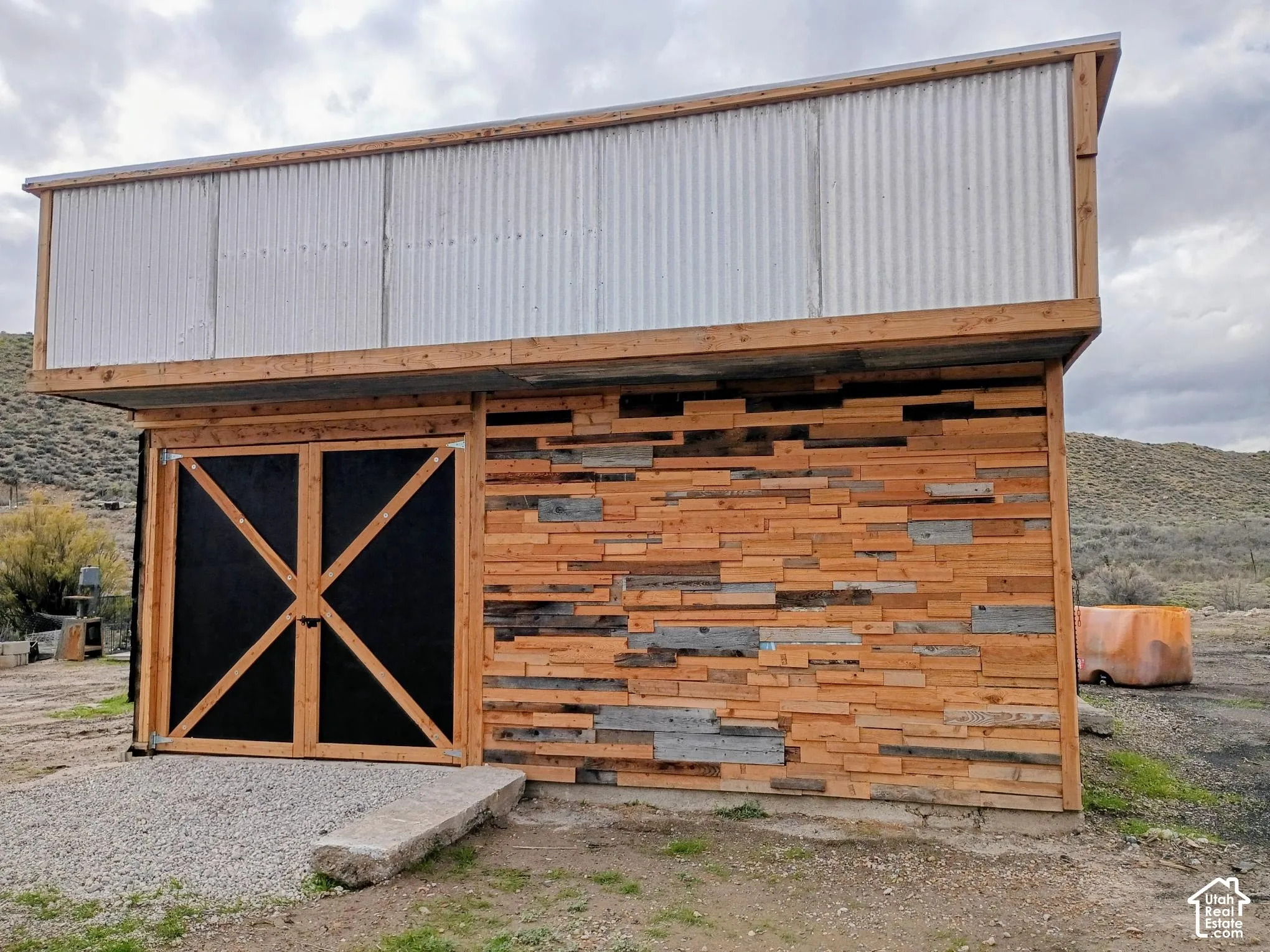 Outbuilding featuring corrugated metal upper siding, wood-plank exterior cladding, and double doors with wood framing