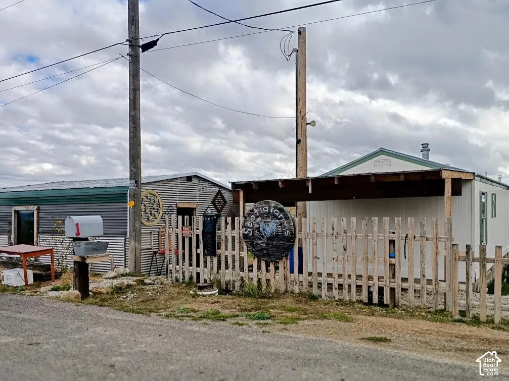 Exterior featuring a wood-slat perimeter fence, metal siding, a covered patio structure, and a gravel lot