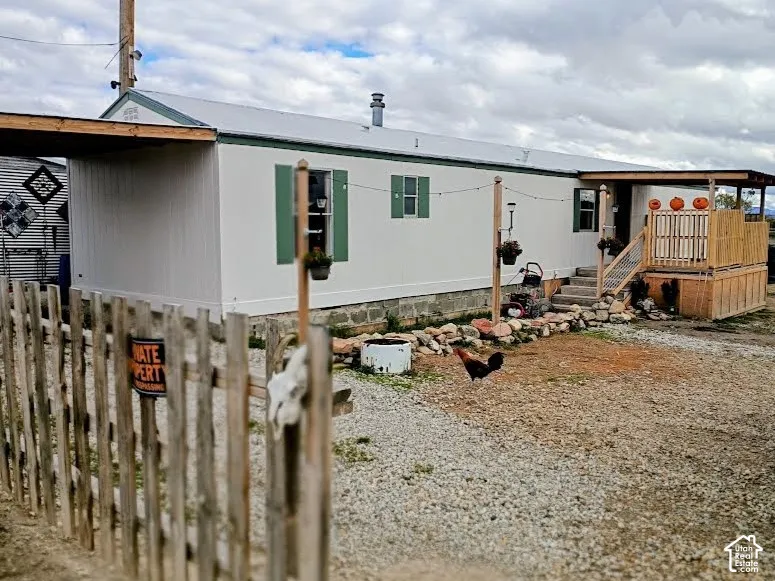 Exterior featuring light-colored vertical siding, decorative shutters, a metal roof, a raised wood deck, and an integrated carport
