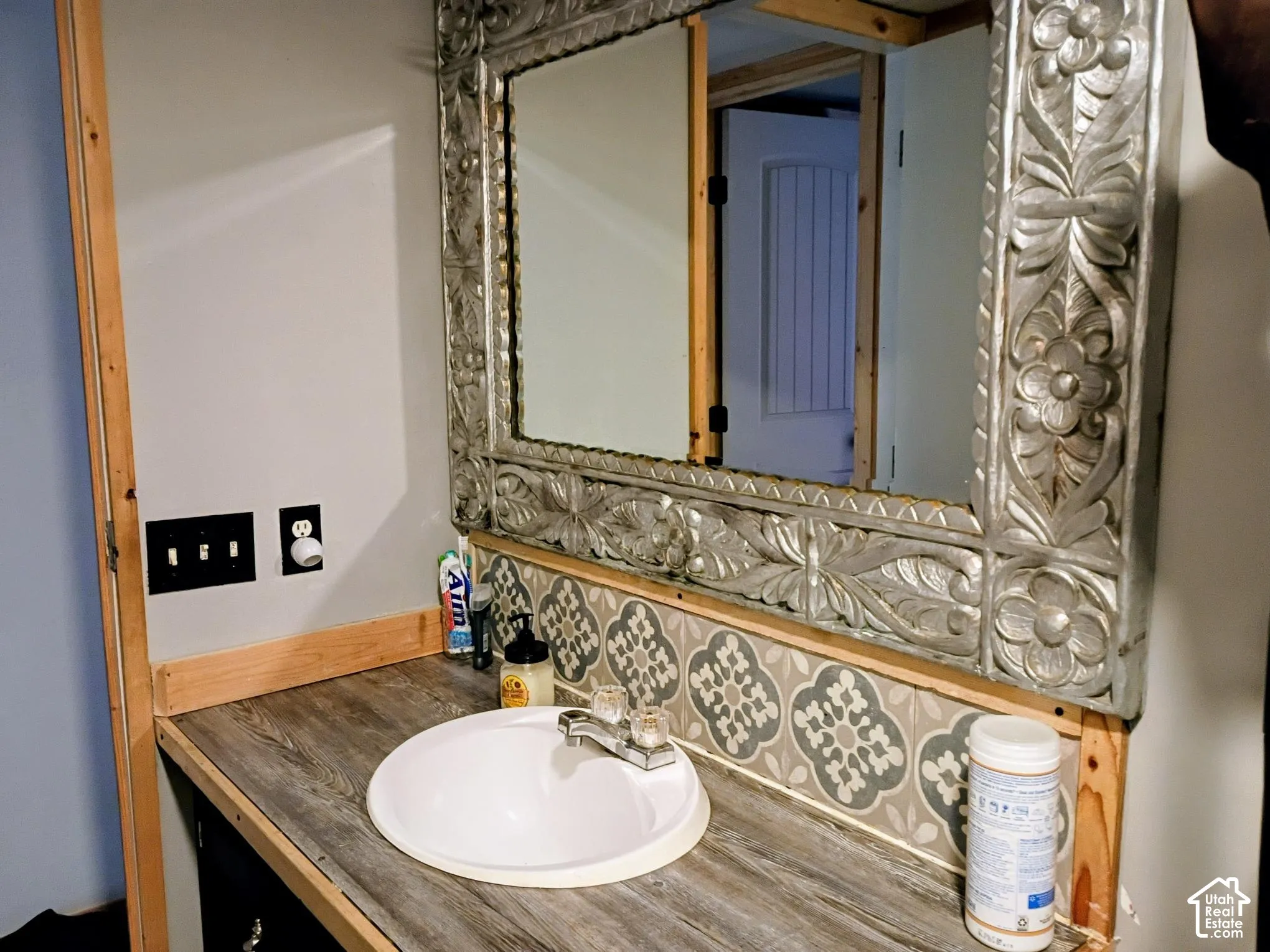 Wood-finish countertop with a recessed white basin, patterned tile backsplash, and decorative metallic framed mirror