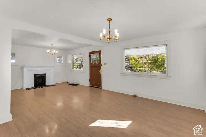 Living area featuring wood-finish flooring, white fireplace mantel, two brass-finish chandeliers, and a multi-pane entry door