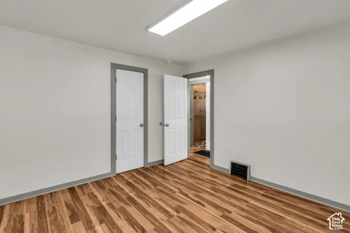 Room featuring wood-finish flooring, neutral walls, two interior six-panel doors, and a rectangular ceiling-mounted light fixture