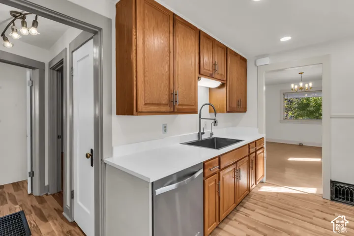 Kitchen featuring warm-tone wood cabinetry, solid-surface countertops, a stainless steel undermount sink with a high-arch faucet, a stainless steel dishwasher, and light wood-finish flooring
