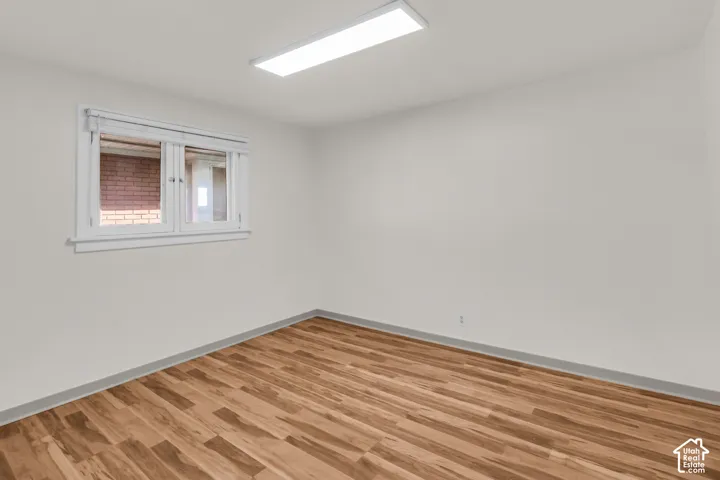 Neutral-toned room featuring wood-finish flooring, a rectangular flush-mount ceiling light fixture, and a window with horizontal blinds