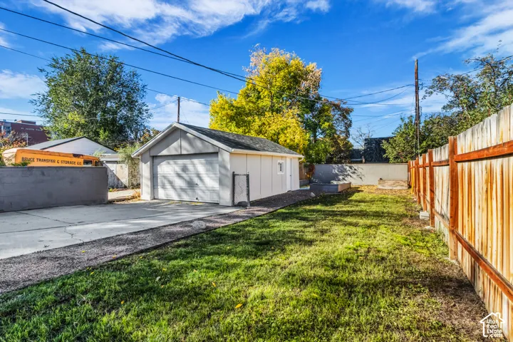 Detached single-car garage featuring a shingled roof, concrete driveway, wood-paneled privacy fencing, and a grass-covered backyard