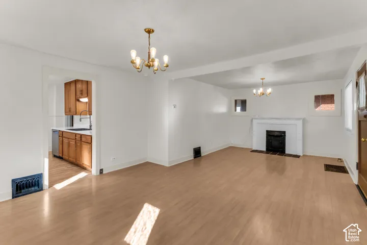 Interior space featuring wood-finish flooring, a white-mantel fireplace with a dark-tiled hearth, dual multi-arm chandeliers, and natural wood kitchen cabinetry