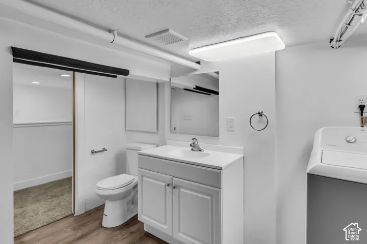 Bathroom featuring a white vanity cabinet with a solid surface countertop, an undermount sink, a wall-mounted rectangular mirror, and wood-finish flooring