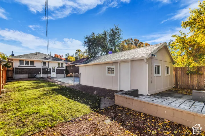 Detached exterior structure with a gable roof, manicured lawn, concrete patio, and wood-panel fencing