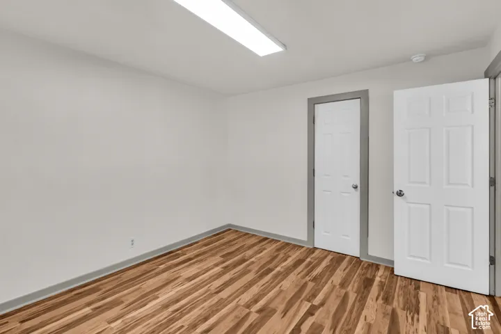 Room featuring wood-finish flooring, neutral wall paint, a flush-mount rectangular light fixture, and six-panel interior doors with grey trim