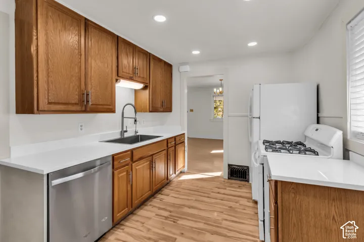 Kitchen featuring medium-tone wood cabinetry, solid-surface countertops, stainless steel undermount sink with arched faucet, recessed ceiling lighting, and wood-finish flooring