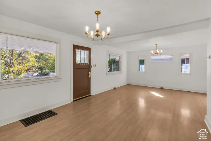 Open living space featuring wood-finish flooring, two multi-arm chandeliers, and an exterior door with a glass inlay panel